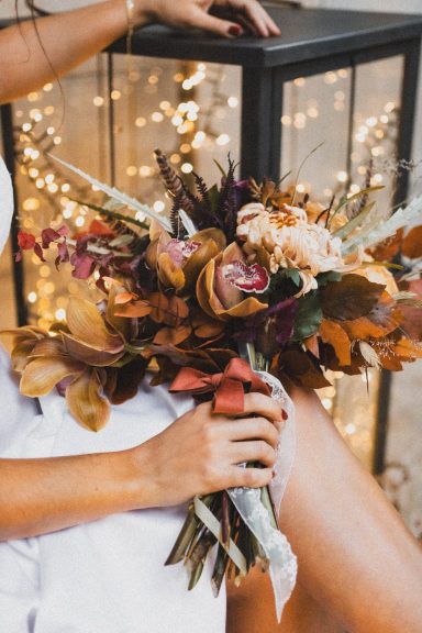 Bouquet automnal coloré avec des fleurs et des feuilles, tenu par une personne en vêtements clairs.