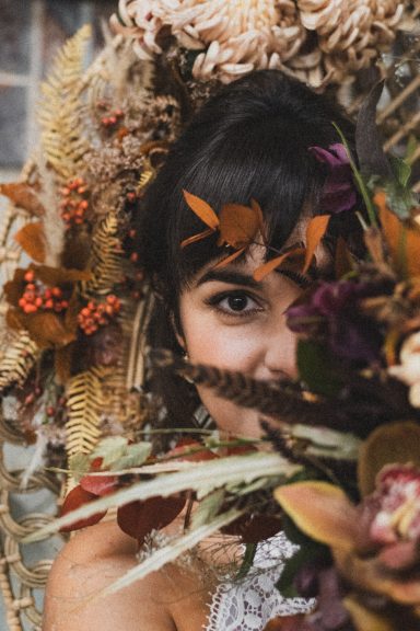 Femme devant un bouquet de fleurs séchées, avec des feuilles orange dans les cheveux.