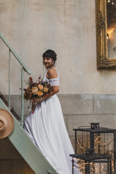 Femme en robe de mariée blanche tenant un bouquet, descendant un escalier.