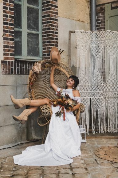 Femme en robe de mariée assise sur une balançoire, tenant un bouquet de fleurs.