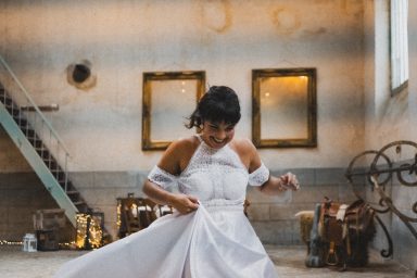 Femme en robe blanche ajustant sa tenue dans un espace lumineux avec des miroirs et une escaliers.